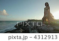 Young woman standing on rocks by the sea with breeze blowing her dress 4312913