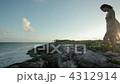 Young woman standing on rocks by the sea with breeze blowing her dress 4312914
