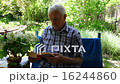An elderly man sitting and reading a book in her  16244860
