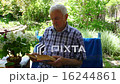 An elderly man sitting and reading a book in her  16244861
