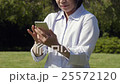 處理有草的資深婦女智能手機在一個刷新的陽光公園 25572120