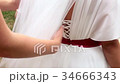 Bridesmaid checking lacing on bride's dress 34666343