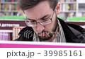 Young brunette black-haired man with glasses looking books on the bookshelves in the bookstore. 39985161