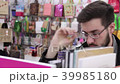 Young brunette black-haired man with glasses looking books on the bookshelves in the bookstore. 39985180