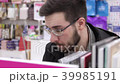 Young brunette black-haired man with glasses looking books on the bookshelves in the bookstore. 39985191