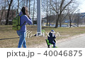 A young mother and a boy are walking outside. The kid skates sitting on the scooter 40046875