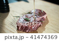 Young cook is watering beef steak with sauce in kitchen of bar. 41474369