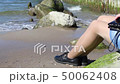 young woman sitting on a stone by the sea 50062408
