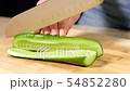 Young woman slicing cucumber with a large knife. 54852280