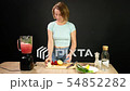A young woman is cooking raw gazpacho. Put vegetables in a blender. 54852282