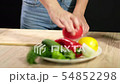 A young woman is cooking raw gazpacho. A young woman cuts a ripe tomato. 54852298