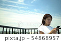 Japanese woman operating mobile phone with smile under blue sky (left copy space) 54868957