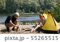 A man makes a fire near the tent. A young girl is watching him. Tourism, travel, green tourism 55265515