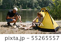 A man chopping wood near the tent. The girl pours tea from a thermos. Hiking, travel, green tourism 55265557