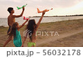 Sisters and their brother running on coast and playing with toy planes 56032178