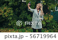 Blonde in gray coat doing selfies on smartphone in autumnal park 56719964