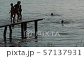 silhouettes of people run on the bridge at sunset and jump into the lake_closer 57137931