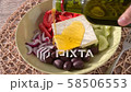 Pouring olive oil onto Greek salad with feta cheese, Kalamata olives, cucumber, tomato, red onion 58506553