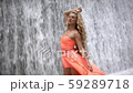 Young woman in dress standing inside big waterfall. Wet girl with curly blonde hair 59289718