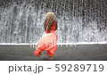Young woman in orange dress coming to big waterfall. Back view of unrecognizable girl 59289719