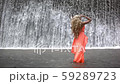 Young beautiful woman standing near big waterfall. Girl in orange dress enjoying moment. 59289723
