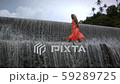 Young serious woman with curly blonde hair in orange dress walking on top of big waterfall. 59289725