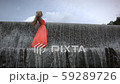 Young woman in orange dress walking on top of big waterfall. Green forest and palms on background.  59289726