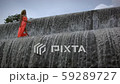 Young woman with curly hair in orange dress walking on top of big waterfall.  59289727