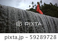Young beautiful woman with curly blonde hair in orange dress walking on top of big waterfall.  59289728