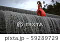 Young beautiful woman with curly blonde hair in orange dress walking on top of big waterfall.  59289729