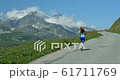 A pretty young woman running up a European Alpine mountain road in summer. 61711769