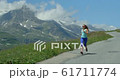 A young woman running down an Alpine road in the French Alps in summertime. 61711774
