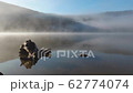 Morning fog in autumn lake landscape. Mountain with trees reflecting in the water 62774074