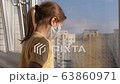 Quarantine, threat of coronavirus. Sad child in protective medical mask sits on windowsill and looks out window. Virus protection, pandemic, prevention epidemic. 63860971