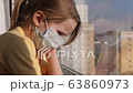 Quarantine, threat of coronavirus. Sad child in protective medical mask sits on windowsill and looks out window. Virus protection, pandemic, prevention epidemic. 63860973