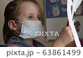 Quarantine, the threat of coronavirus. A child in a medical mask sits at a table and cuts out of paper. Quarantine homework. 63861499