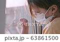 Quarantine, threat of coronavirus. Sad child in protective medical mask sits on windowsill and looks out window. Virus protection, pandemic, prevention epidemic. 63861500