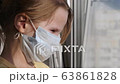 Quarantine, threat of coronavirus. Sad child in protective medical mask sits on windowsill and looks out window. Virus protection, pandemic, prevention epidemic. 63861828