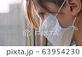 Quarantine, threat of coronavirus. Sad child in protective medical mask sits on windowsill and looks out window. Virus protection, pandemic, prevention epidemic. 63954230