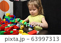 3 years old girl playing with coloured blocks of a constructor. The child develops his thinking skills. Development and education of preschoolers. 63997313