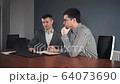 Communicating colleagues sharing laptop in office 64073690