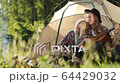 Happy young couple sitting on the nature near tent and campfire, chill, guy playing on a guitar and sings. The girl drinks tea or coffee from a metal cup. Forest camping. FullHD Footage. Smiling faces 64429032