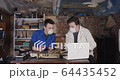 Two young student scientists in protective respiratory masks working in an old dirty workshop garage with some electronics soldering and watching instructions on laptop while speaking to each other 4K 64435452