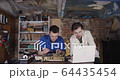 Two young student scientists working in an old dirty workshop garage with some electronics soldering and watching instructions on laptop while speaking to each other 4K 64435454