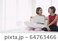 Two asian woman sitting on bed and use laptop computer surfing social media talking. 64763466