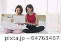 Two asian woman sitting on bed and use laptop computer surfing social media talking. 64763467