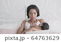 Mother carried her baby and worked through the laptop on the bed. 64763629