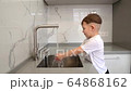 a little boy washes his hands in the kitchen sink 64868162