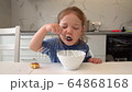 little girl eating porridge in the kitchen 64868168