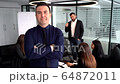Confident young man holding arms folded while standing at the table with talking colleagues on a background 64872011